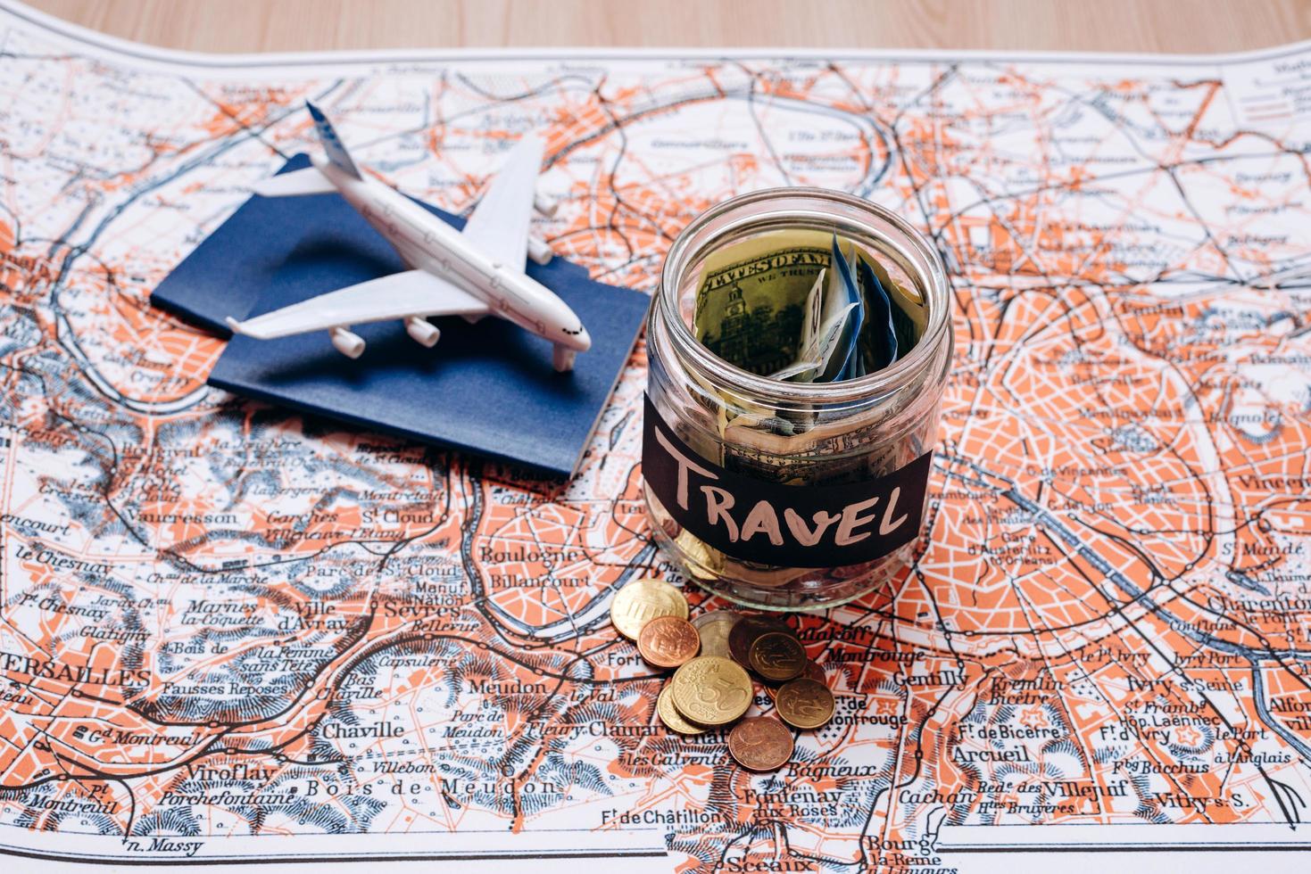 Urlaubsbudget-Konzept. Feiertagsgeldeinsparungen in einem Glasgefäß mit Flugzeugspielzeug auf der Weltkarte foto