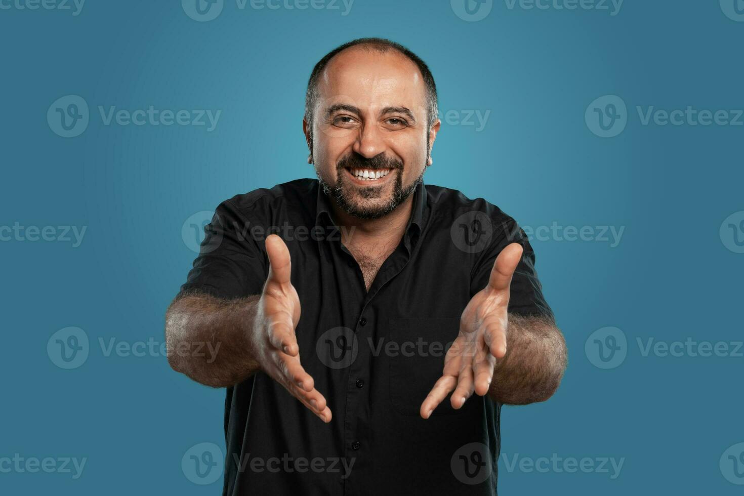 Nahansicht Porträt von ein brünett mittleren Alters Mann mit Bart, gekleidet im ein schwarz T-Shirt und posieren gegen ein Blau Hintergrund. foto