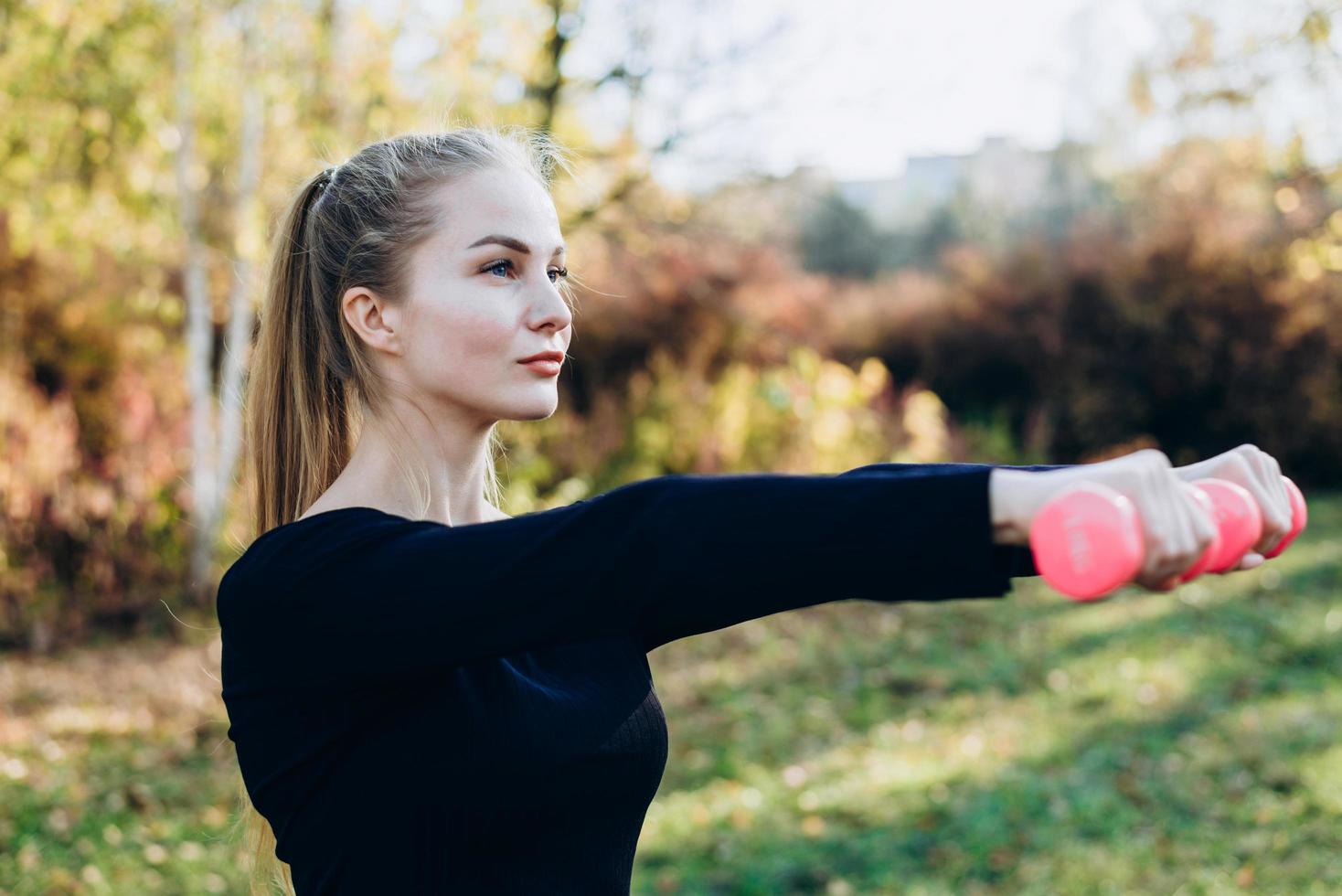 glückliches Fitness-Frauentraining mit Hanteln im Freien. Mädchen, das im Sommer freie Gewichte hebt. foto