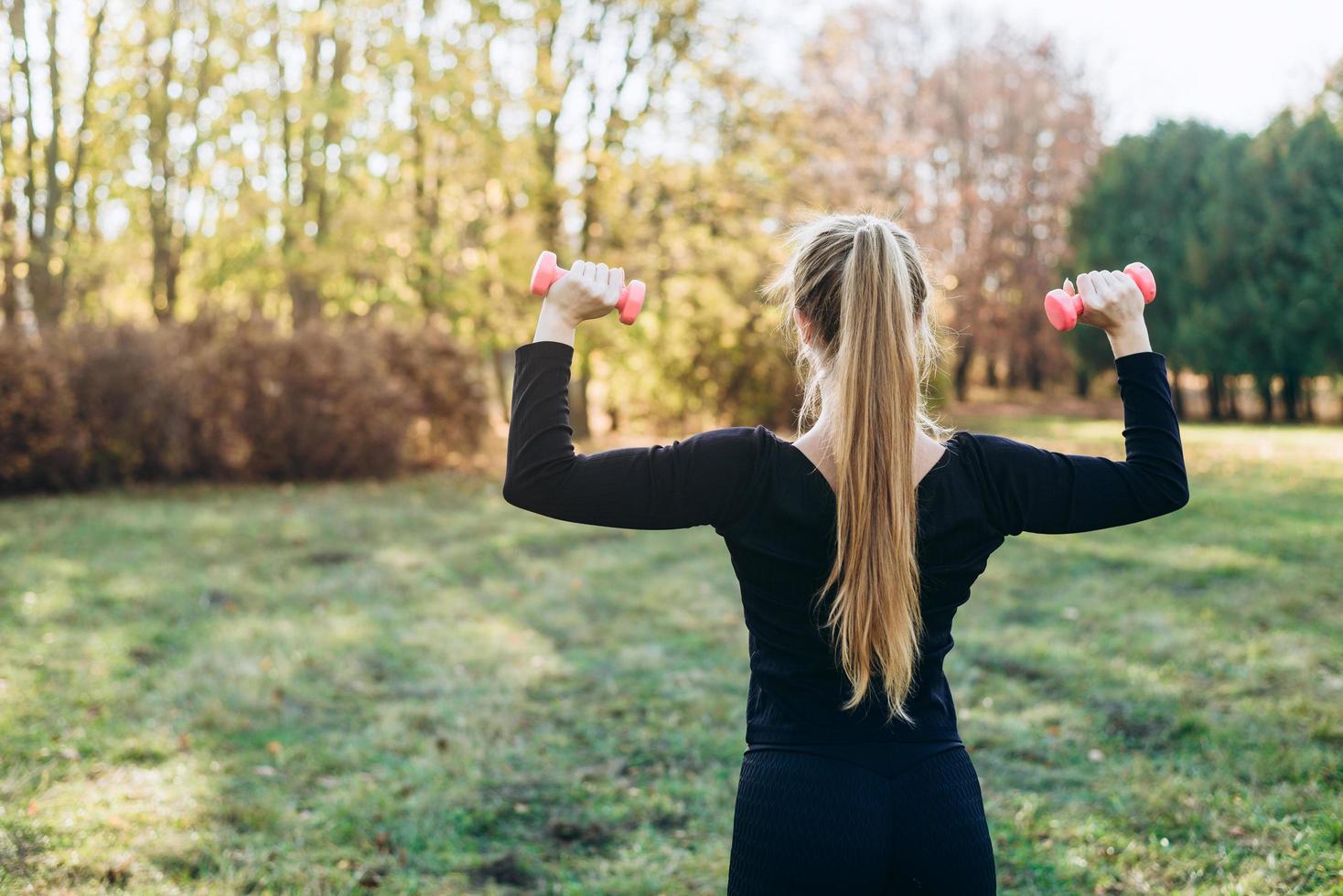 Fitness im Park, Mädchen mit Hanteln, Rückansicht. foto