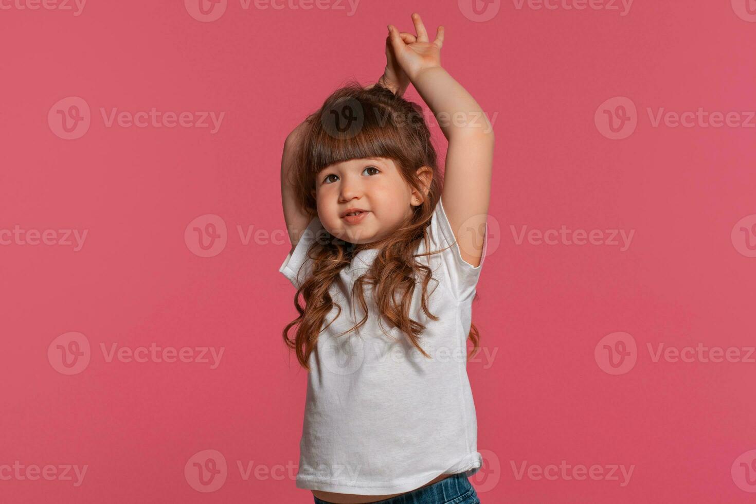 Nahansicht Porträt von ein wenig Brünette Mädchen gekleidet im ein Weiß T-Shirt posieren gegen ein Rosa Studio Hintergrund. aufrichtig Emotionen Konzept. foto