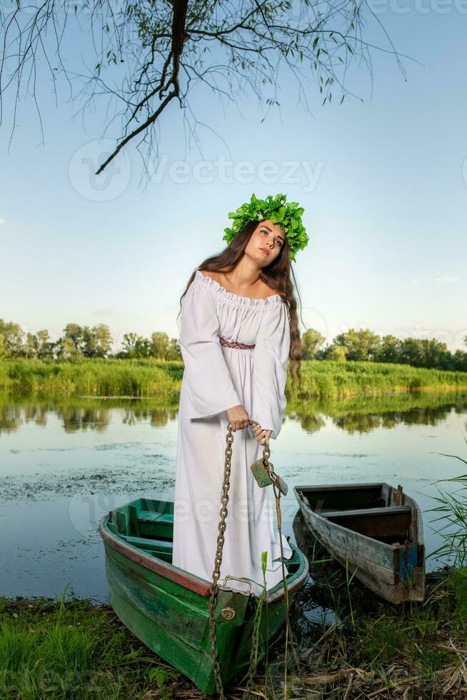 jung Frau mit Blume Kranz auf ihr Kopf, entspannend auf Boot auf Fluss beim Sonnenuntergang. Konzept von weiblich Schönheit, sich ausruhen im das Dorf foto