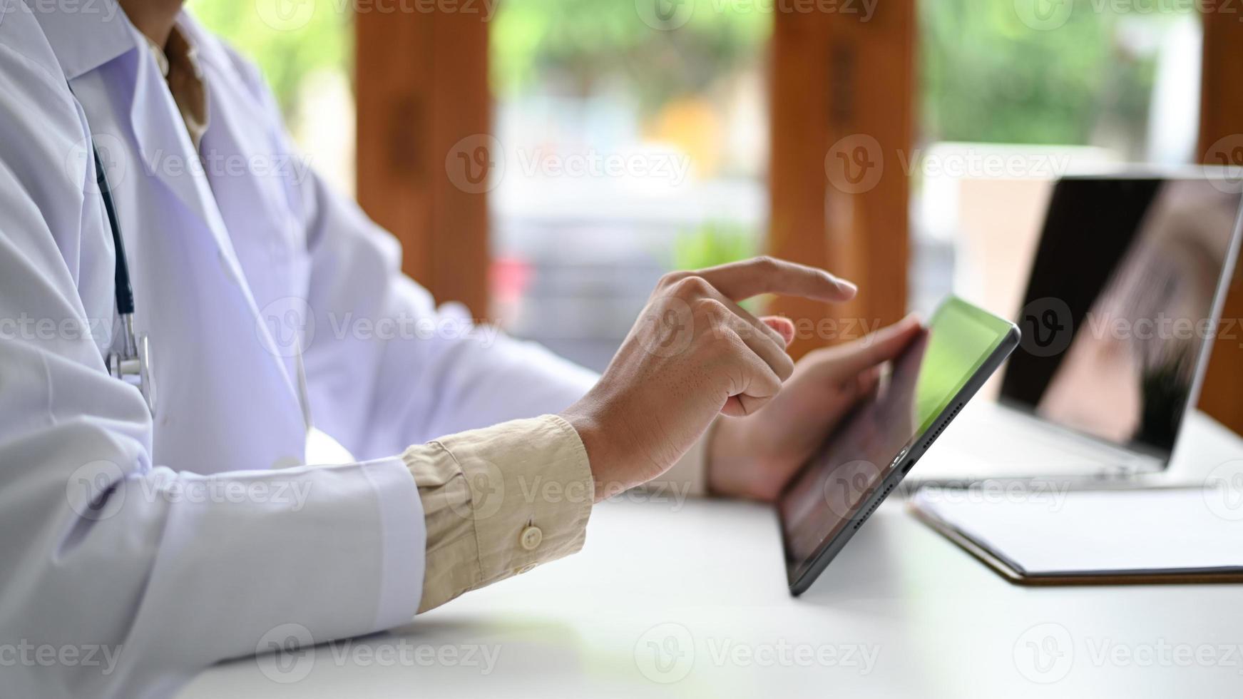 Ein Mann in einem Laborkittel hält und bedient ein Tablet, ein Mediziner in einem Laborkittel verwendet ein Tablet, seitliches Foto. foto