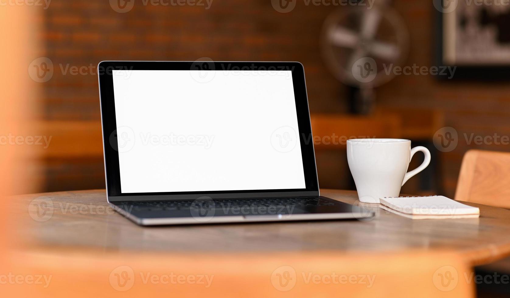 Mockup-Laptop mit leerem Bildschirm mit Kaffee und Notebook auf dem Tisch, von vorne aufgenommen. foto