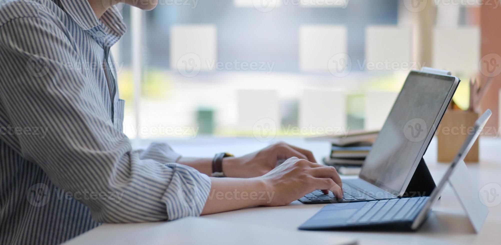 Ausgeschnittene Aufnahme eines Mannes, der einen Laptop und ein digitales Tablet in einem modernen Büro verwendet. foto