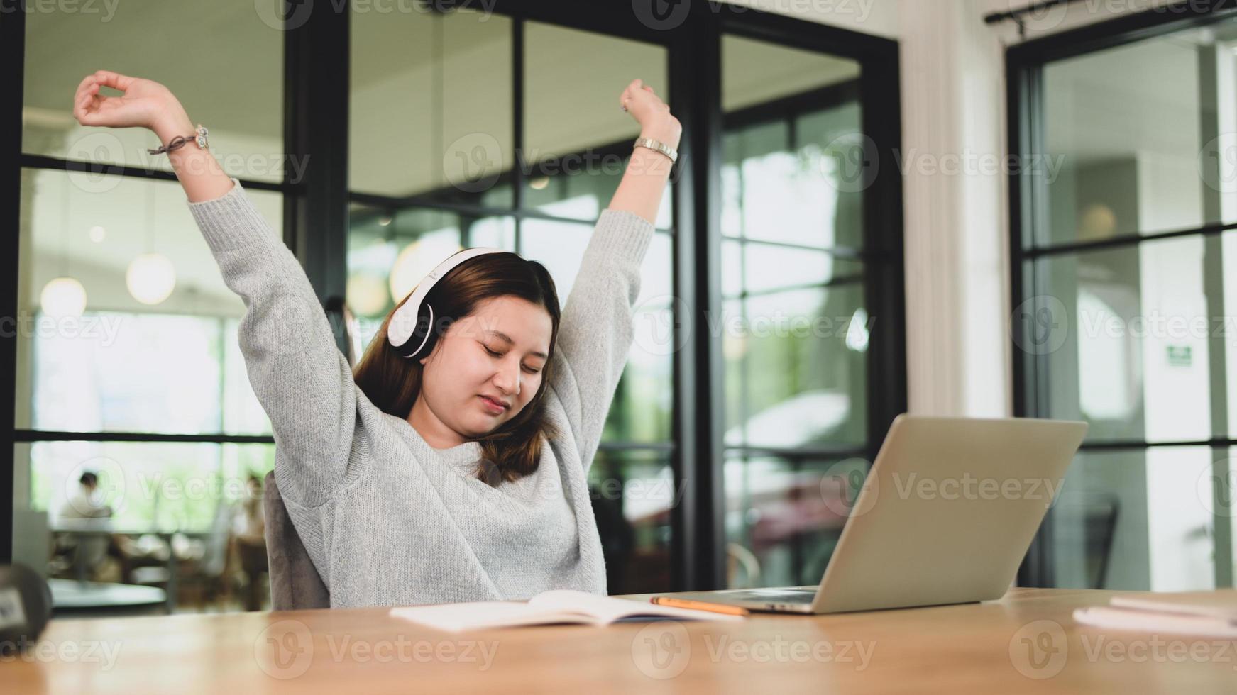 Ein junges Mädchen trägt Kopfhörer mit erhobenen Armen, um sich während eines Online-Kurses zu entspannen. foto