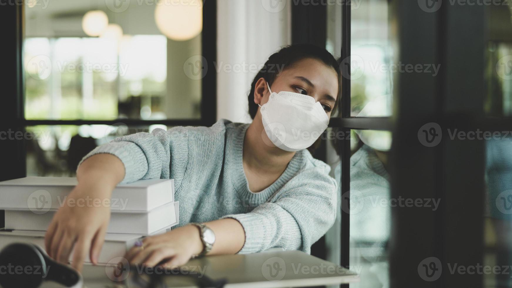 Eine asiatische Studentin, die eine medizinische Maske trägt, sitzt am Fenster und schaut heraus. foto