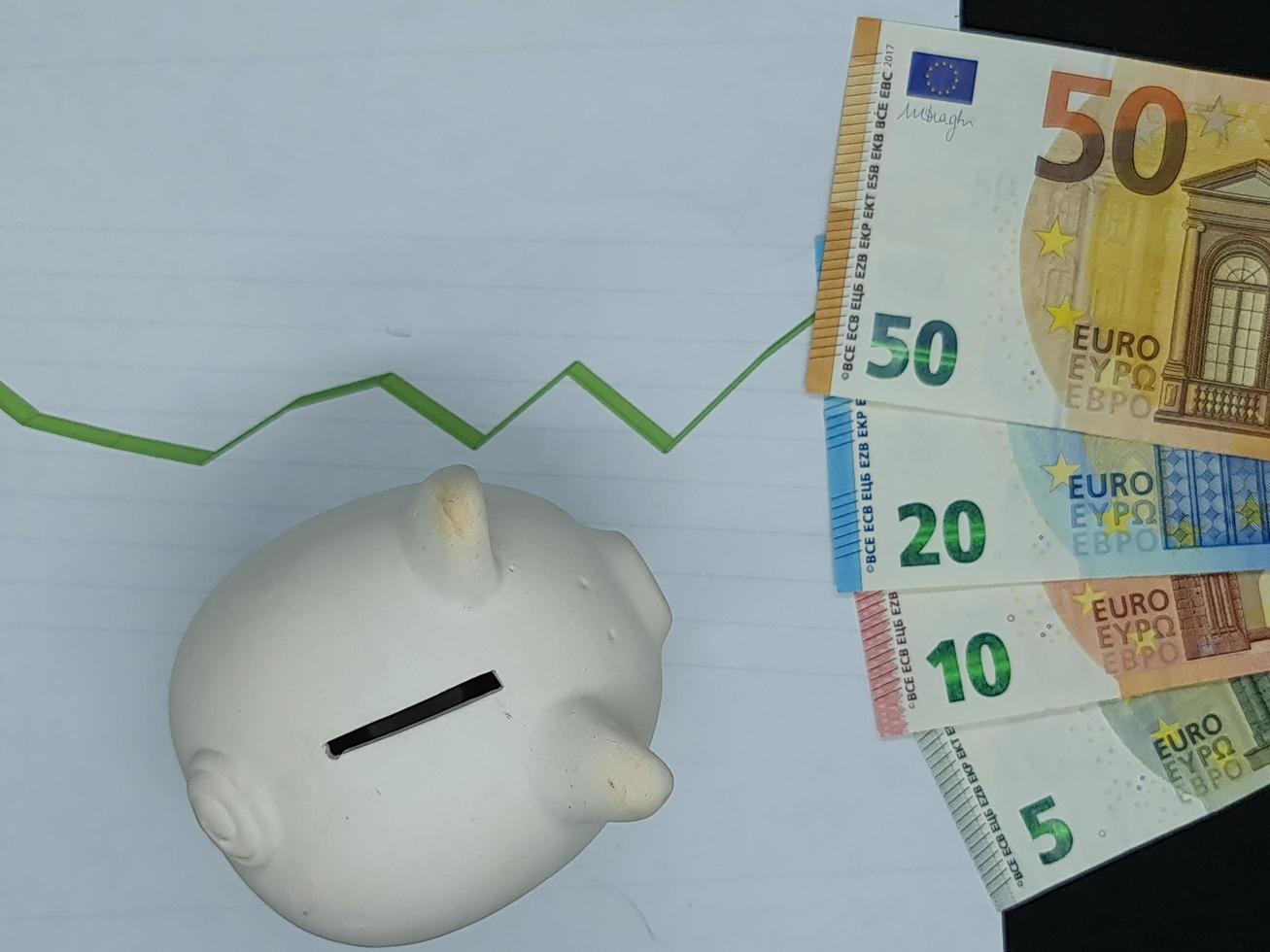 Europäische Banknoten und Sparschwein im Hintergrund mit ansteigender grüner Trendlinie, Ansicht von oben foto