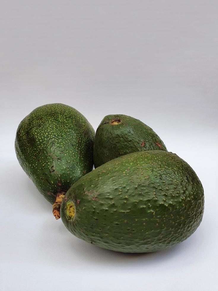 drei frische Avocados mit Haut auf der weißen Oberfläche, Avocado natürlichen Ursprungs zur Zubereitung vegetarischer Speisen foto