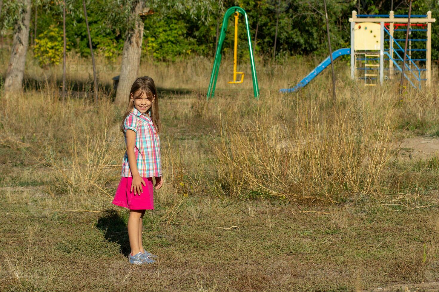 glücklich kaukasisch wenig Mädchen von 6 7 Jahre lächelnd und suchen beim Kamera auf Spielplatz im Herbst Zeit foto
