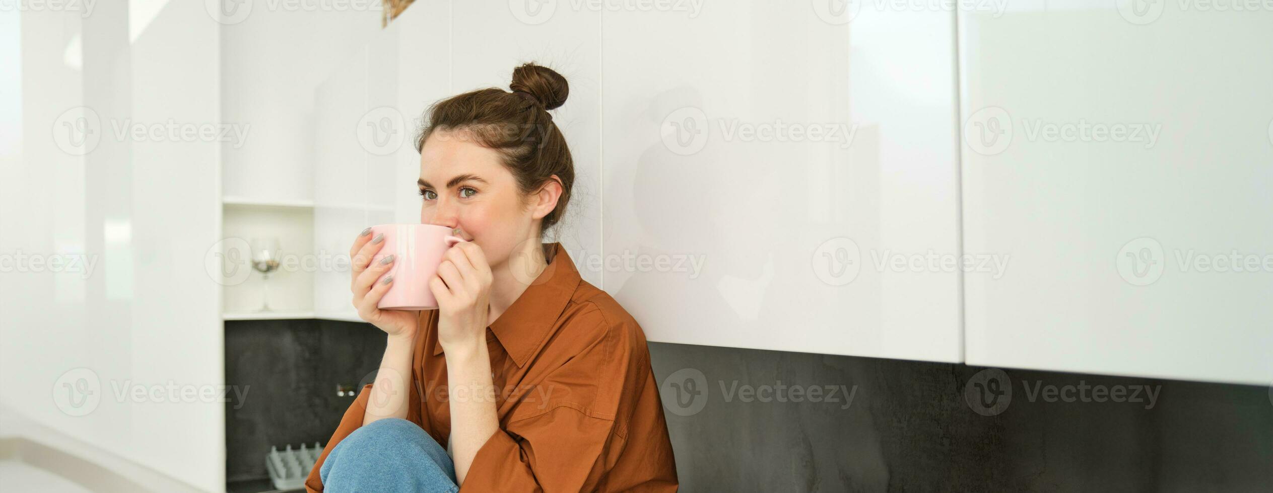 Porträt von jung Frau mit Tasse von Kaffee, sitzt im Küche und Getränke aromatisch trinken beim heim, hält Tee Becher foto