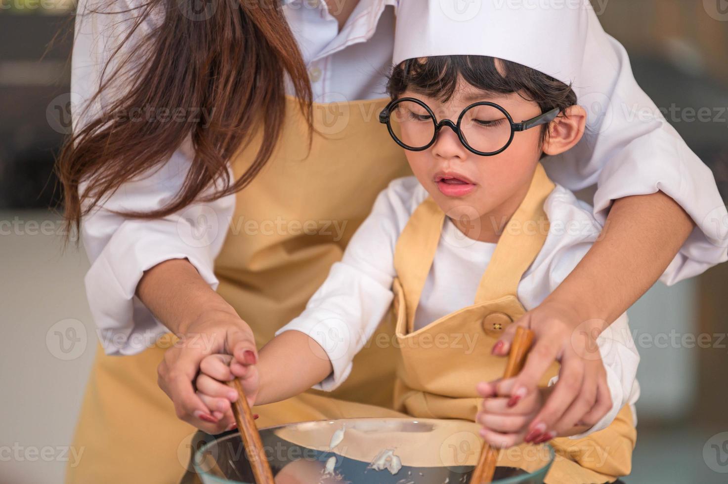 glücklicher süßer kleiner Junge mit Brille und schöne asiatische Mutter bereiten sich auf das Kochen in der Küche zu Hause vor. Menschen Lebensstil und Familie. Konzept für hausgemachte Speisen und Zutaten. zwei thailänder leben foto
