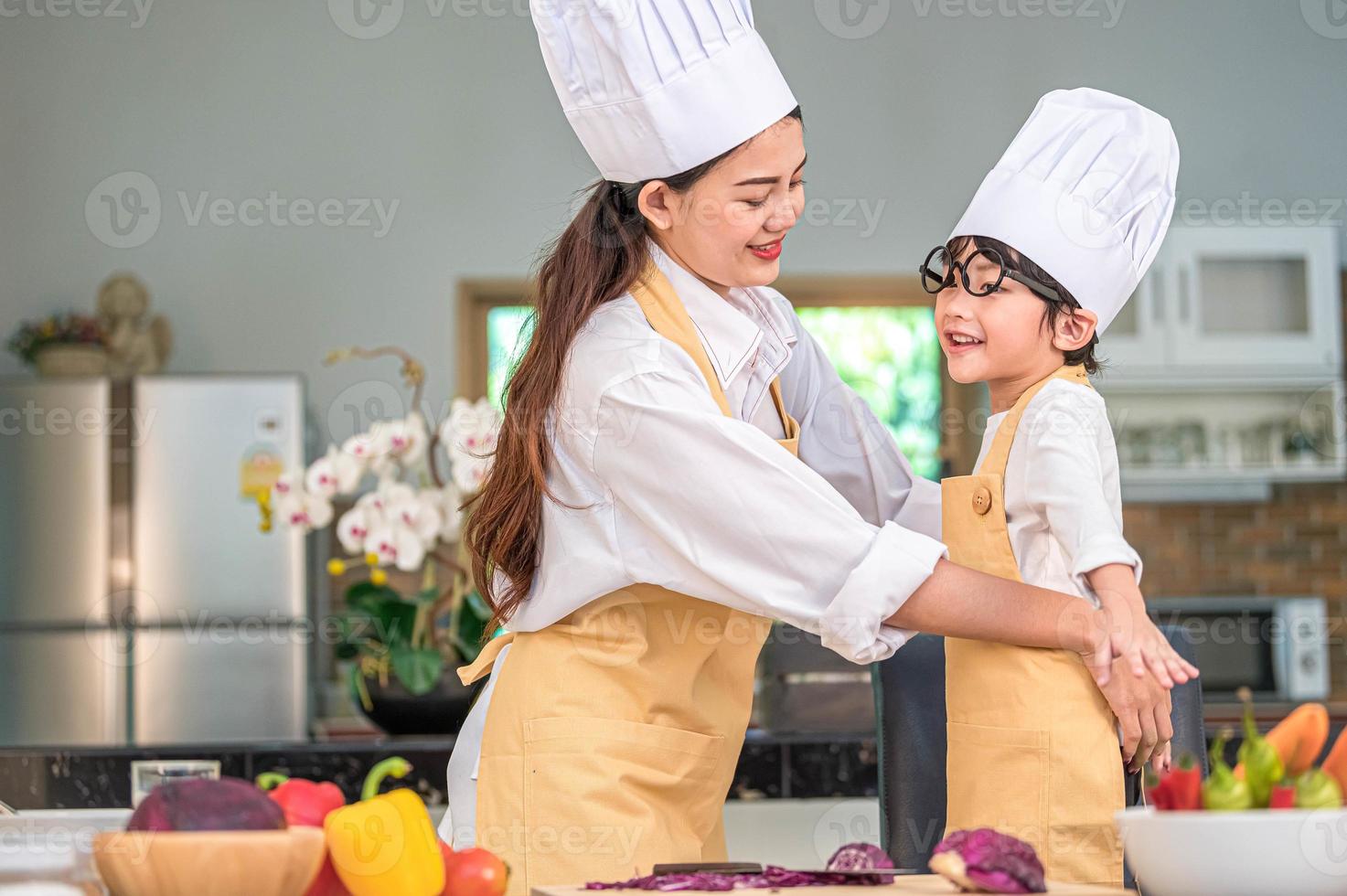 glückliche schöne asiatische frau verkleidet süße kleine junge koch-outfit für die vorbereitung zum kochen in der hausküche. Menschen Lebensstil und Familie. Konzept für hausgemachte Speisen und Zutaten. zwei thailänder leben foto