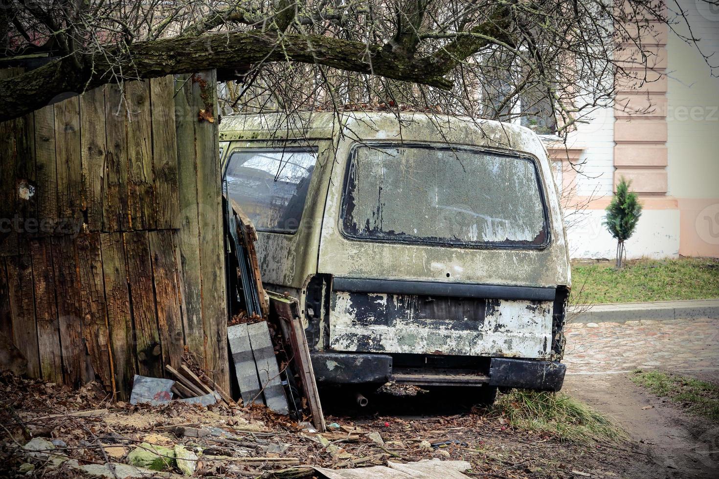 alter kaputter rostiger Lieferwagen in der Nähe von Holzgebäude unter kahlen Baum foto