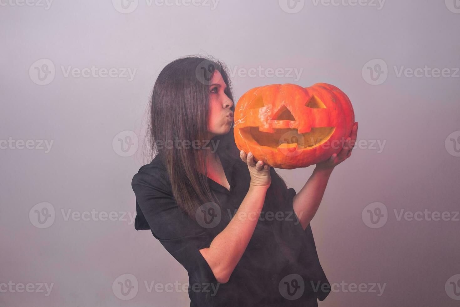 Frau wie Hexe ist Stehen mit das Kürbis im das Studio. Halloween und Karneval Konzept foto