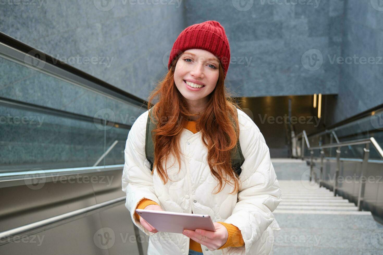 schön Rothaarige weiblich Modell- posieren im Stadt, Gehen oben Treppe mit Digital Tablette, mit Gadget zu planen ihr Route, lesen während gehen irgendwo foto