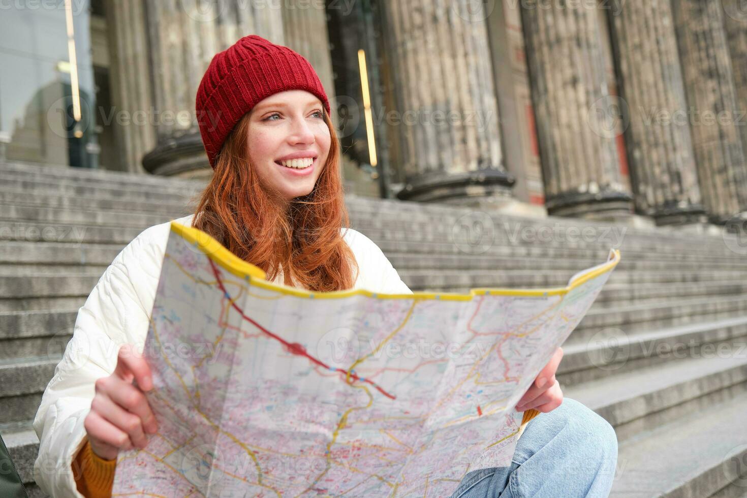 Porträt von jung Rothaarige Frau, Tourist sitzt mit Papier Karte und sieht aus zum ein Route zu Tourismus Attraktion, ruht auf Treppe draußen foto