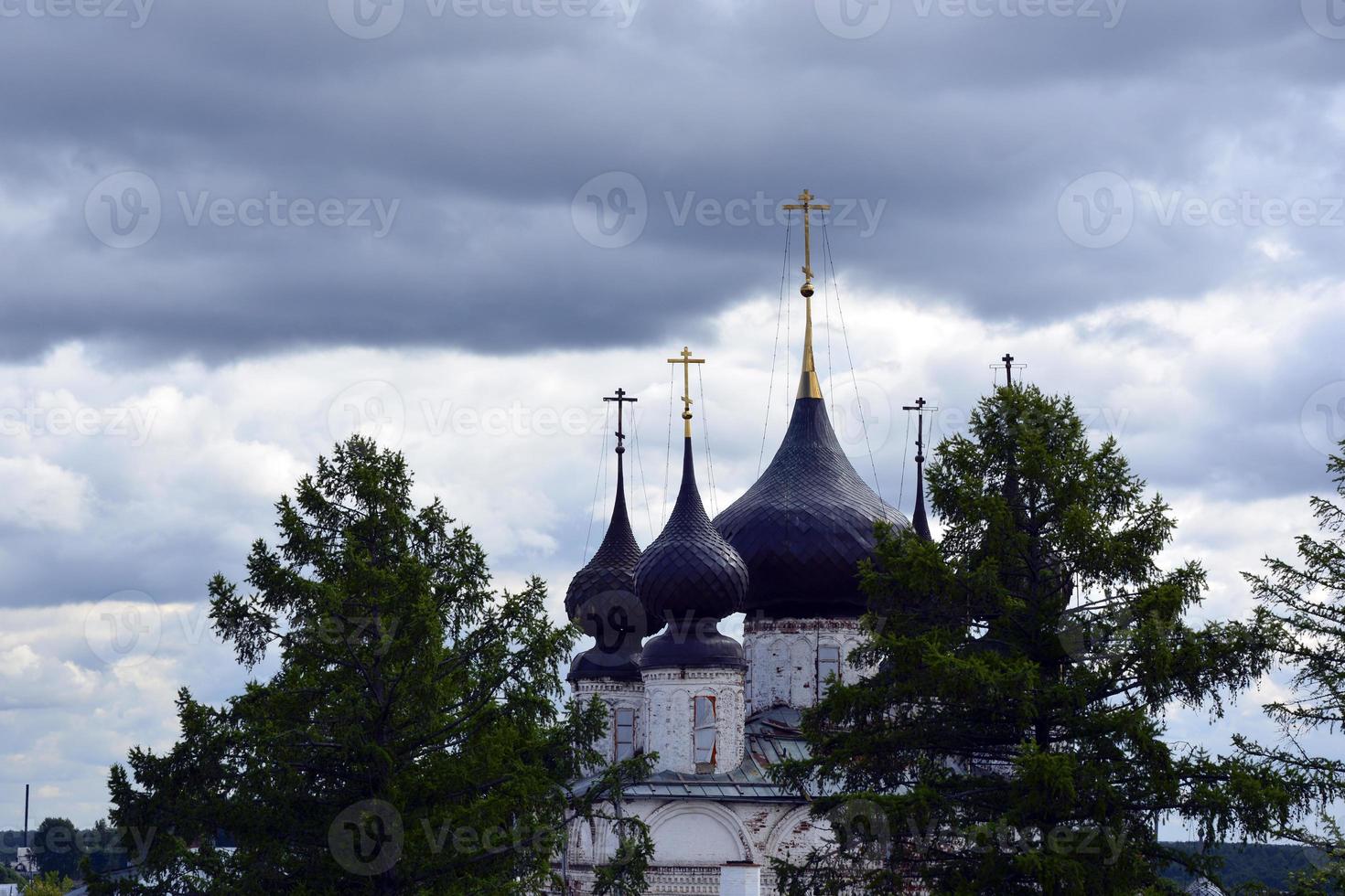 Kirchenkuppeln mit Kreuzen gegen den blauen Himmel. Tempel aus weißem Stein zwischen den Bäumen. foto