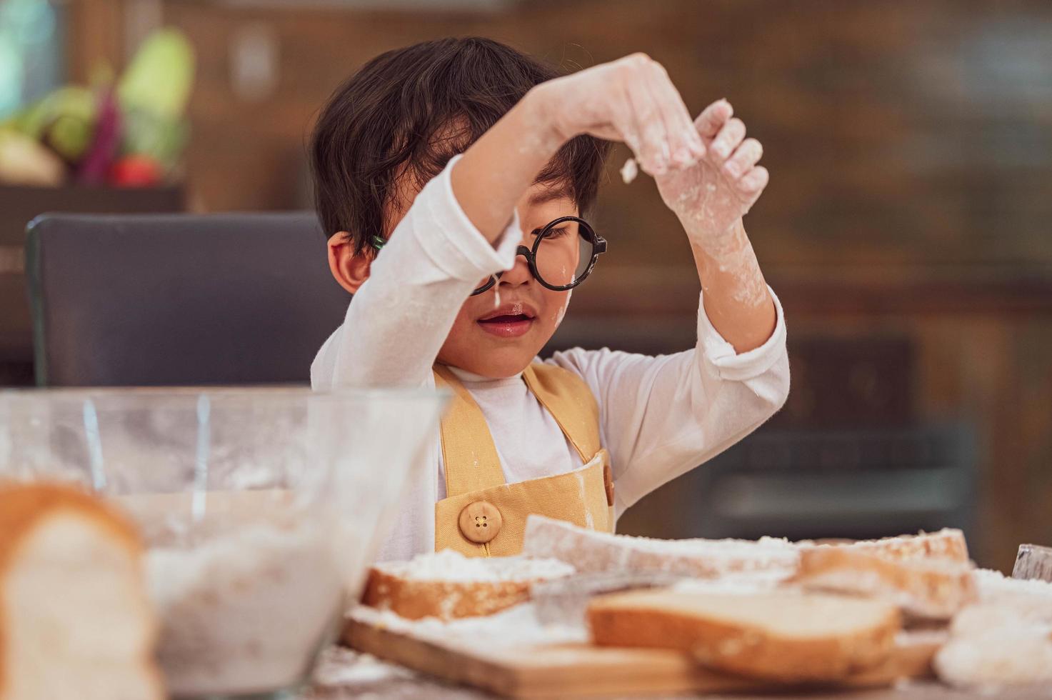 Porträt süßer kleiner asiatischer Glücksjunge, der daran interessiert ist, Bäckerei mit lustigen in der heimischen Küche zu backen. Menschen Lebensstil und Familie. Konzept für hausgemachte Speisen und Zutaten. Weihnachtskuchen und Kekse backen foto