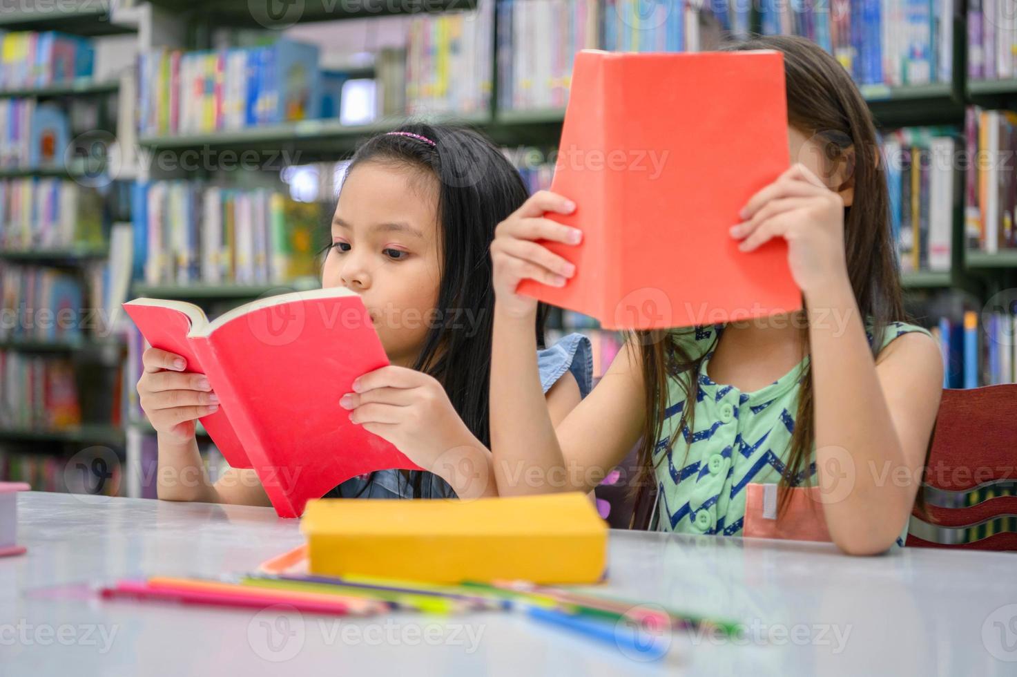 Zwei kleine süße Mädchen, multiethnische Freunde, die zusammen Bücher in der Schulbibliothek lesen. Menschen Lebensstil und Bildung Lernkonzept. glückliche Freundschaftskinder, die Freizeitbeschäftigung für Prüfungstest machen foto