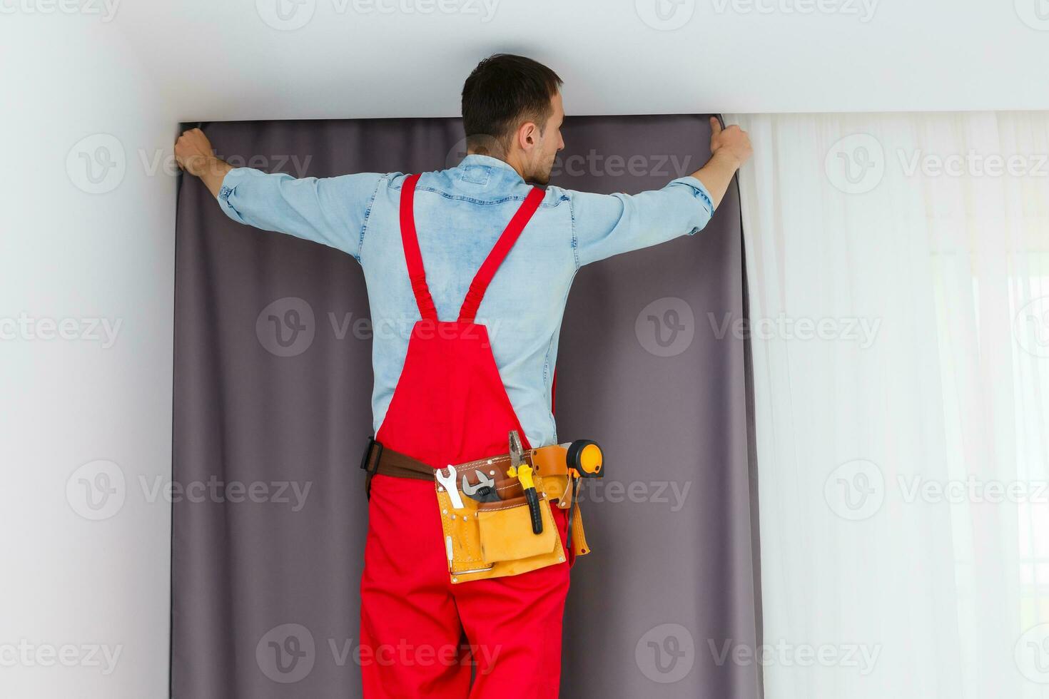 praktisch Mann Zuhause Installation und Reparatur Bedienung Techniker oder Zuhause Inhaber hängend Vorhänge zum das Fenster Behandlung im ein Neu Haus. foto