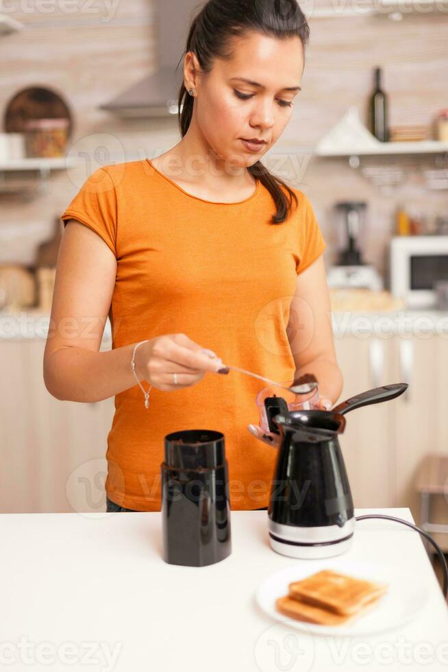 Hausfrau Putten Kaffee im elektrisch Topf während Frühstück. Hausfrau beim Zuhause Herstellung frisch Boden Kaffee im Küche zum Frühstück, Trinken, Mahlen Kaffee Espresso Vor gehen zu Arbeit foto