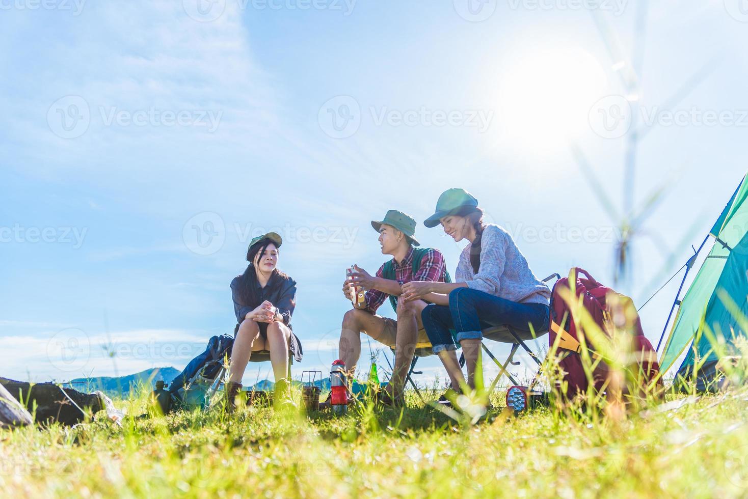 Gruppe von Reisenden, die im Vordergrund der Wiese campen und Picknick machen. Berg- und Seehintergrund. Menschen und Lebensstile Konzept. Outdoor-Aktivität und Freizeitthema. Backpacker- und Wanderer-Lifestyle foto