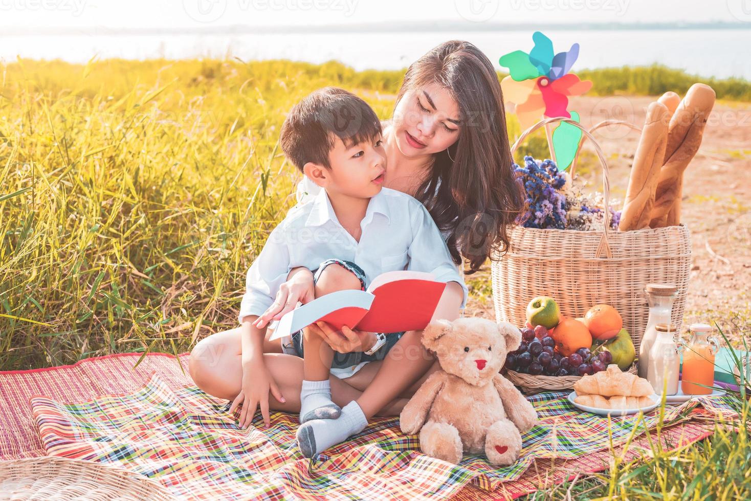 schöne asiatische mutter und sohn machen picknick und lesen geschichten in roten büchern im ostersommerfest auf der wiese in der nähe von see und berg. Urlaub. menschen lebensstil und glückliches familienleben. thailändische Person foto