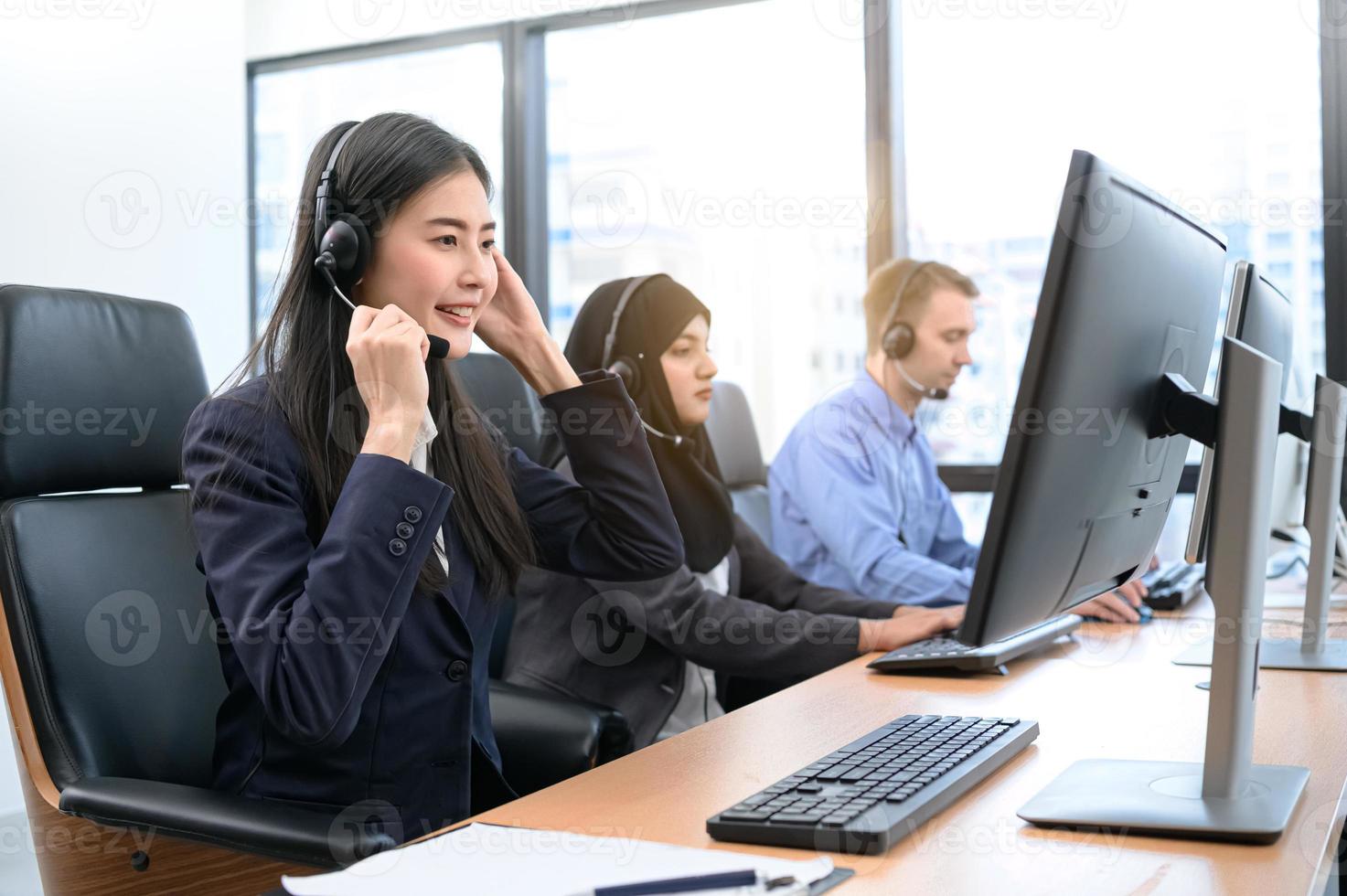 Gruppe junger Berufs-Call-Center-Betreiber mit Headsets, die im Büro arbeiten. Business-Telemarketing-Service-Mitarbeiter, die sich auf die Gesprächsarbeit konzentrieren und kundenfreundlich sprechen foto