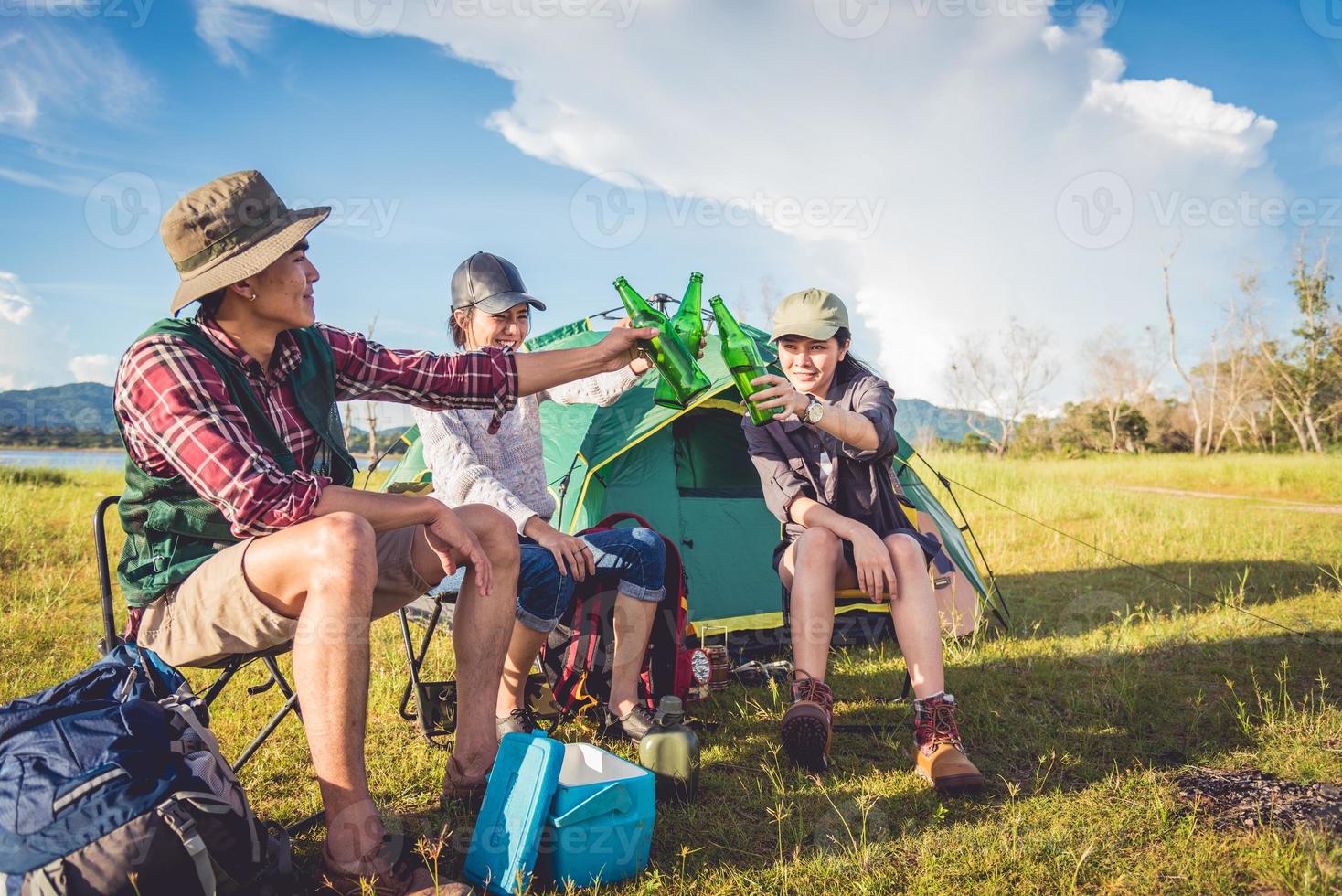 Gruppe von Reisenden, die campen und Picknick auf der Wiese mit Zeltvordergrund machen. Berg- und Seehintergrund. Menschen und Lebensstile Konzept. Outdoor-Aktivität und Freizeitthema. Backpacker- und Wanderer-Thema foto