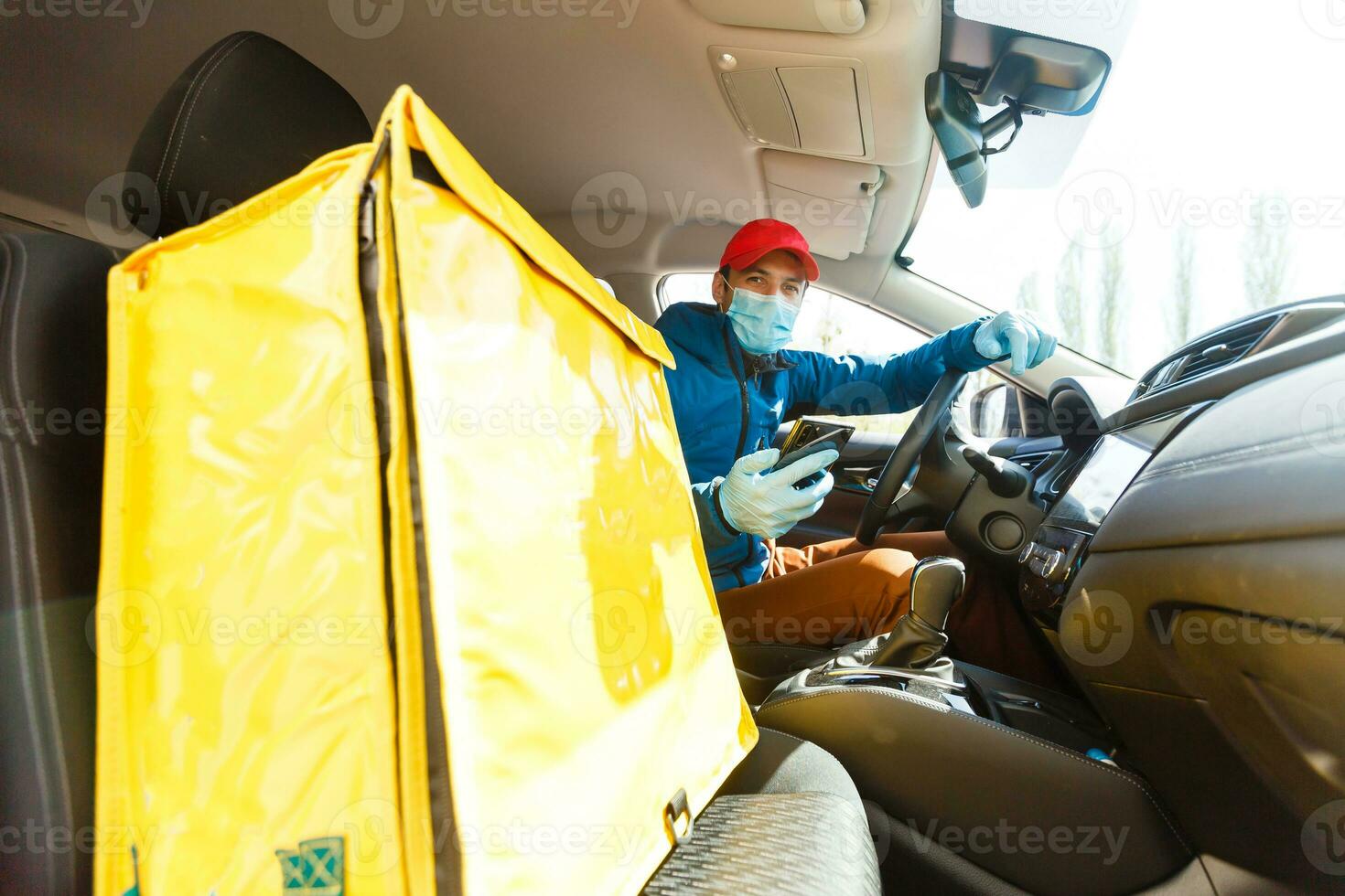 Essen Lieferung Mann im ein schützend Maske und Handschuhe mit ein thermo Rucksack in der Nähe von ein Auto während das Quarantäne Zeitraum foto