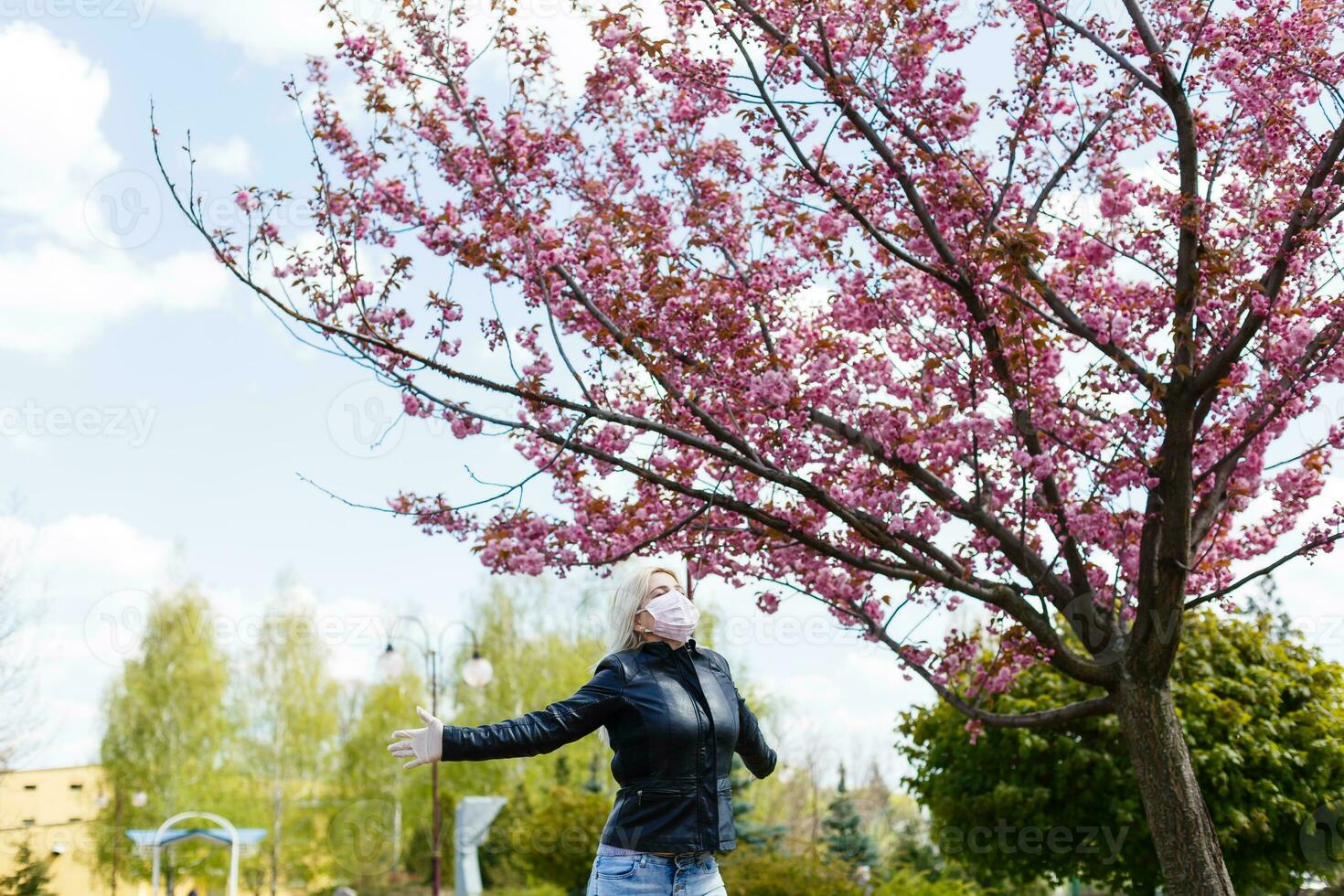 glücklich jung Frau tragen Gesichts- Maske zum Virus Schutz Stehen draußen auf sonnig Frühling Tag. foto