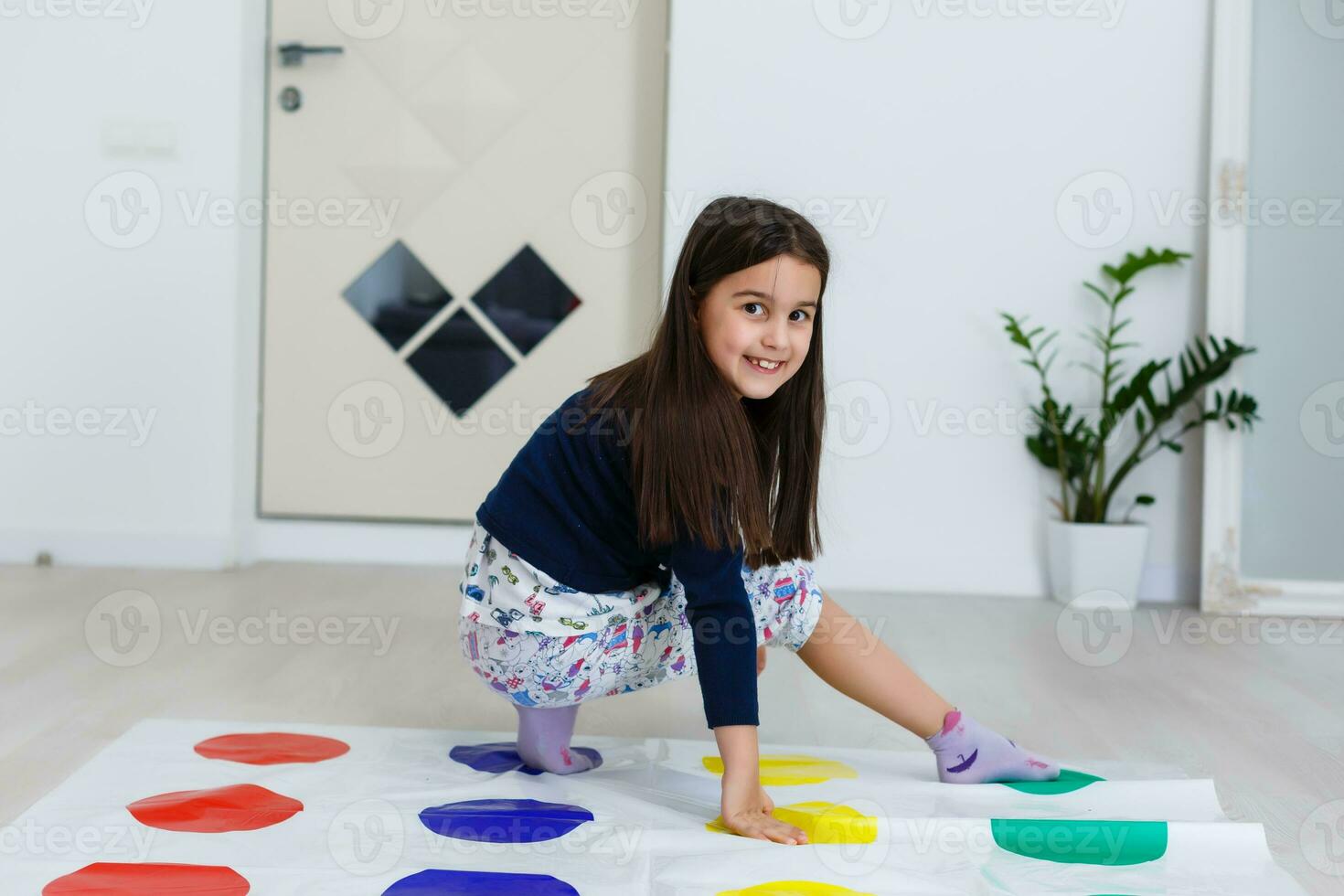 wenig Mädchen spielen auf ein Twister Spiel beim heim. Mädchen lächelt und sieht aus oben foto