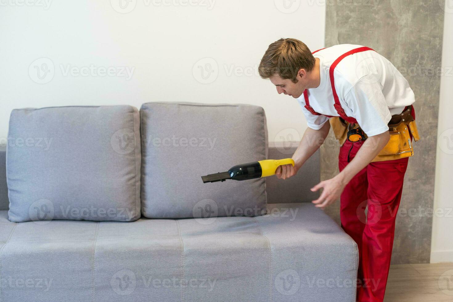 gut aussehend jung Mann Reinigung Möbel. Prozess von tief Möbel Reinigung, entfernen Schmutz von Sofa. Waschen Konzept foto