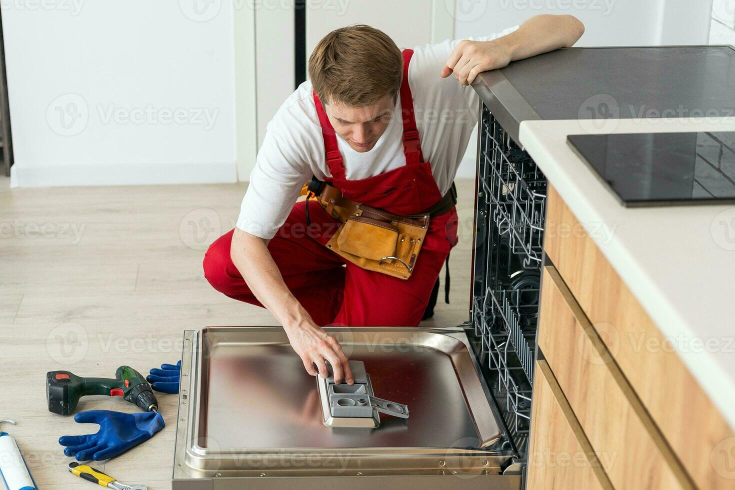 Techniker oder Arbeiter im Uniform installiert Geschirrspüler in das Küche Möbel. Handwerker tragen Arbeiter passen reparieren Instandhaltung von Geschirrspüler. Meister im schützend Handschuhe Fix Geschirrspüler. foto