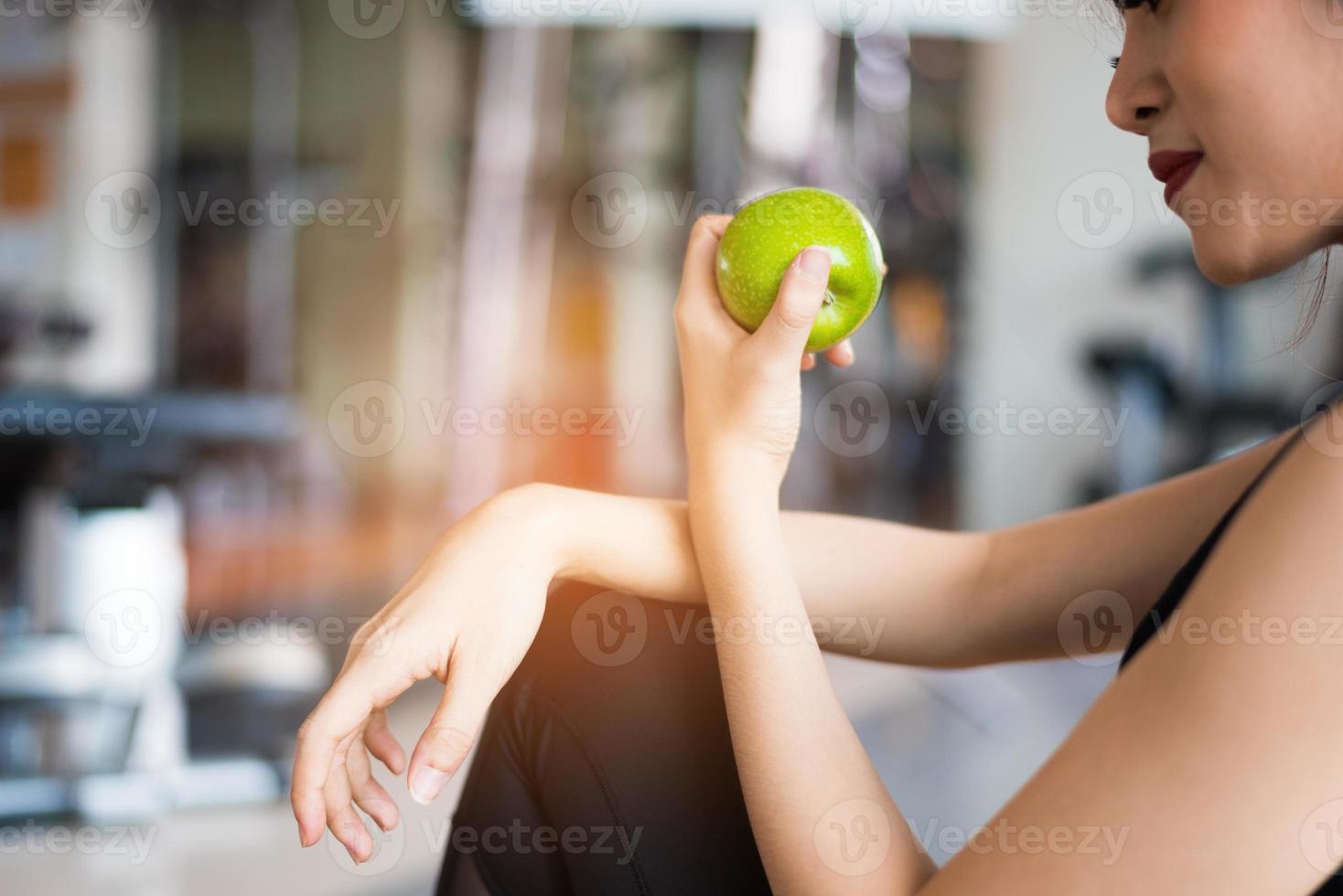 Sportfrau, die grünen Apfel im Fitness-Studio sitzt und isst. Essen und Obst und Ernährungskonzept. Entspannen und sauberes Essenskonzept. Gesundheits- und Trainingsübungsthema foto