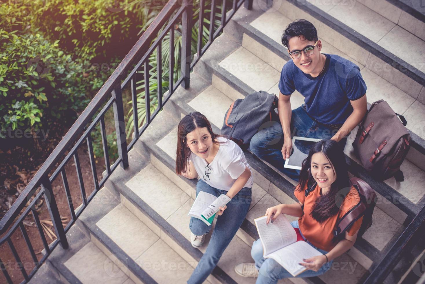 drei junge asiatische campusstudenten genießen es, im treppenhaus nachhilfe zu geben und gemeinsam bücher zu lesen. Freundschafts- und Bildungskonzept. Campus Schule und Universität Thema. Glück und Spaß beim Lernen im College foto