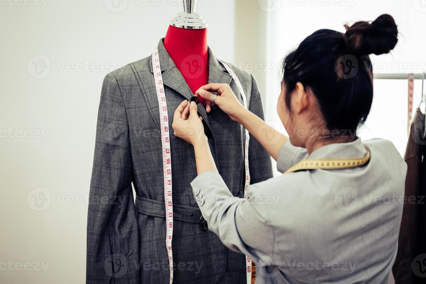 Asiatische Modedesignerin, die sich auf die Uniform des formellen Anzugs auf dem Mannequin-Modell einpasst. Modedesigner stilvoller Showroom. Näh- und Schneiderkonzept. kreative Schneiderin Stylistin foto