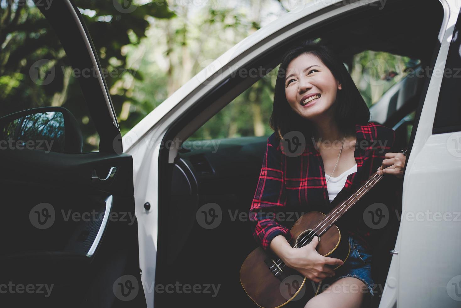 Schönheit asiatische Frau lächelt und hat Spaß im Sommer im Freien mit Ukulele im weißen Auto. Reisen des Fotografenkonzepts. Hipster-Stil und Solo-Frauenthema. Lifestyle und Glück Lebensthema foto