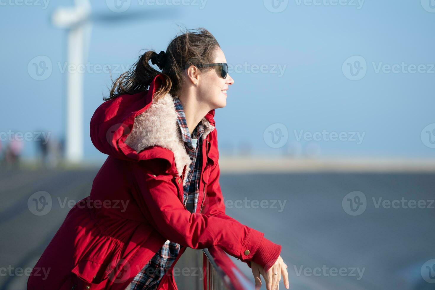 auf das Hintergrund von Windmühlen, ein jung Frau im ein rot Jacke ist genießen ihr Winter Urlaub. foto