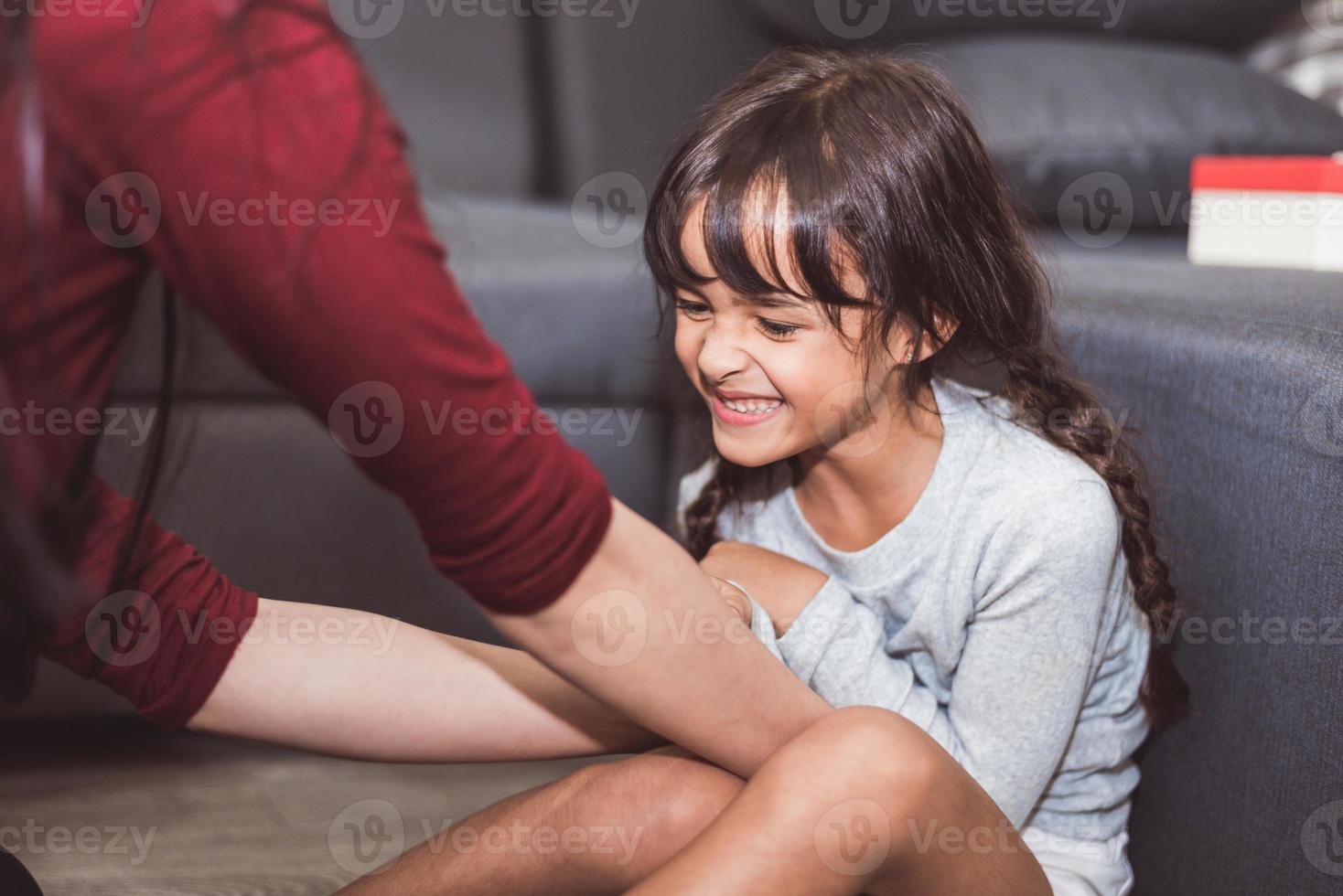 Kaukasisches kleines Mädchen von Mutter im Wohnzimmer gekitzelt. Menschen Lifestyle und Kinderkonzept foto