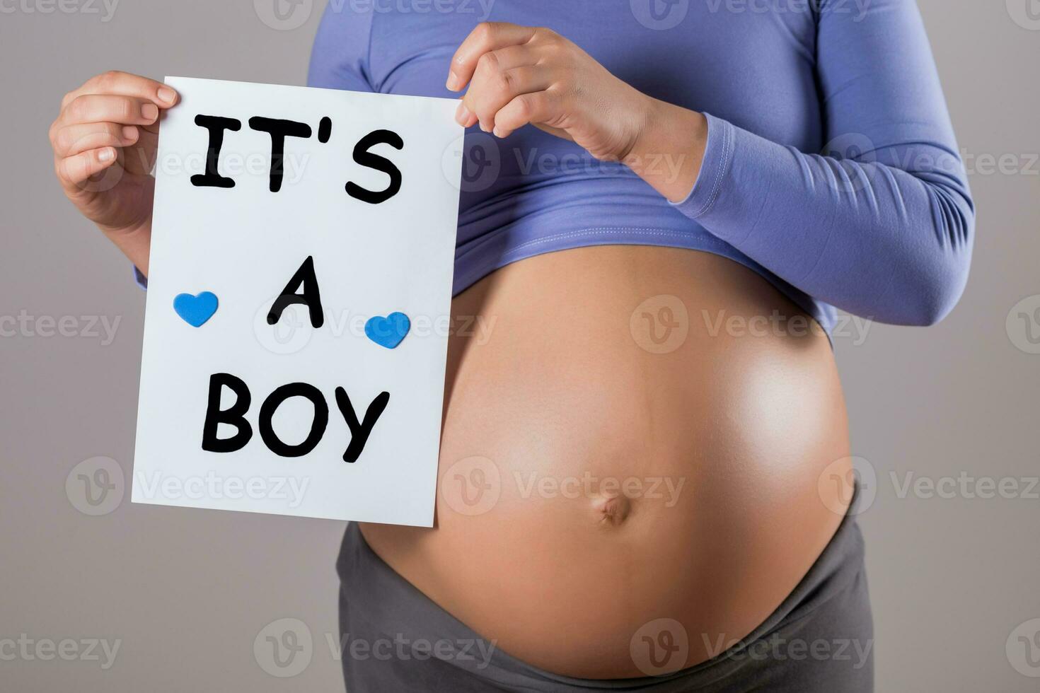 Bild von schließen oben Bauch von schwanger Frau halten Papier mit Text es ist ein Junge auf grau Hintergrund. foto