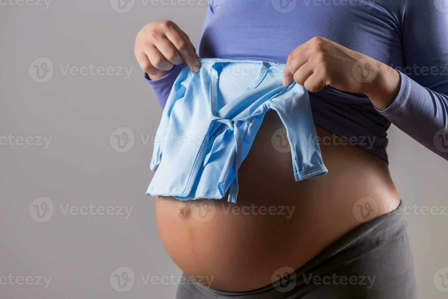 Bild von Bauch von schwanger Frau mit ein Blau T-Shirt zum Baby Junge auf grau Hintergrund. foto