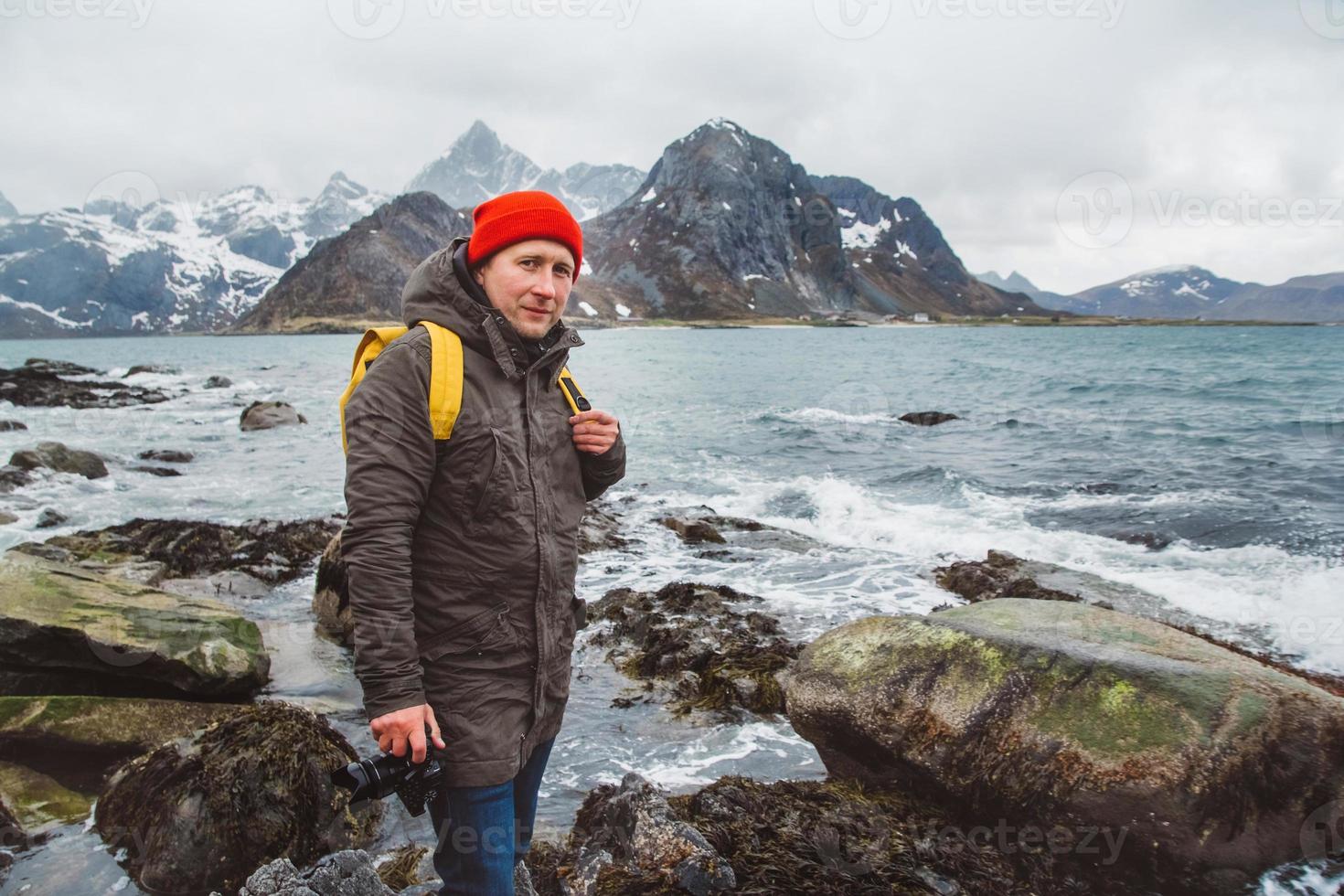 Reisender Fotograf, der auf Felsen vor dem Hintergrund von Meer und Bergen steht foto