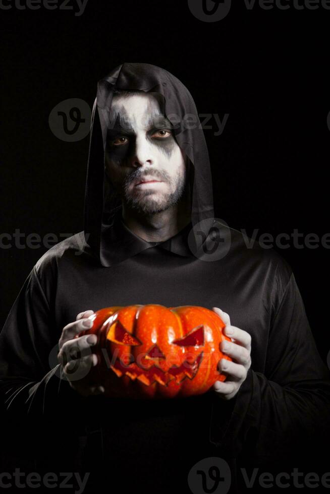 gespenstisch grimmig Sensenmann halten ein Kürbis Über schwarz Hintergrund, Halloween Outfit. foto