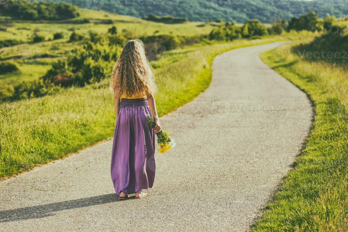 Frau im ein lila Kleid Gehen Nieder ein Straße und halten Blumen foto