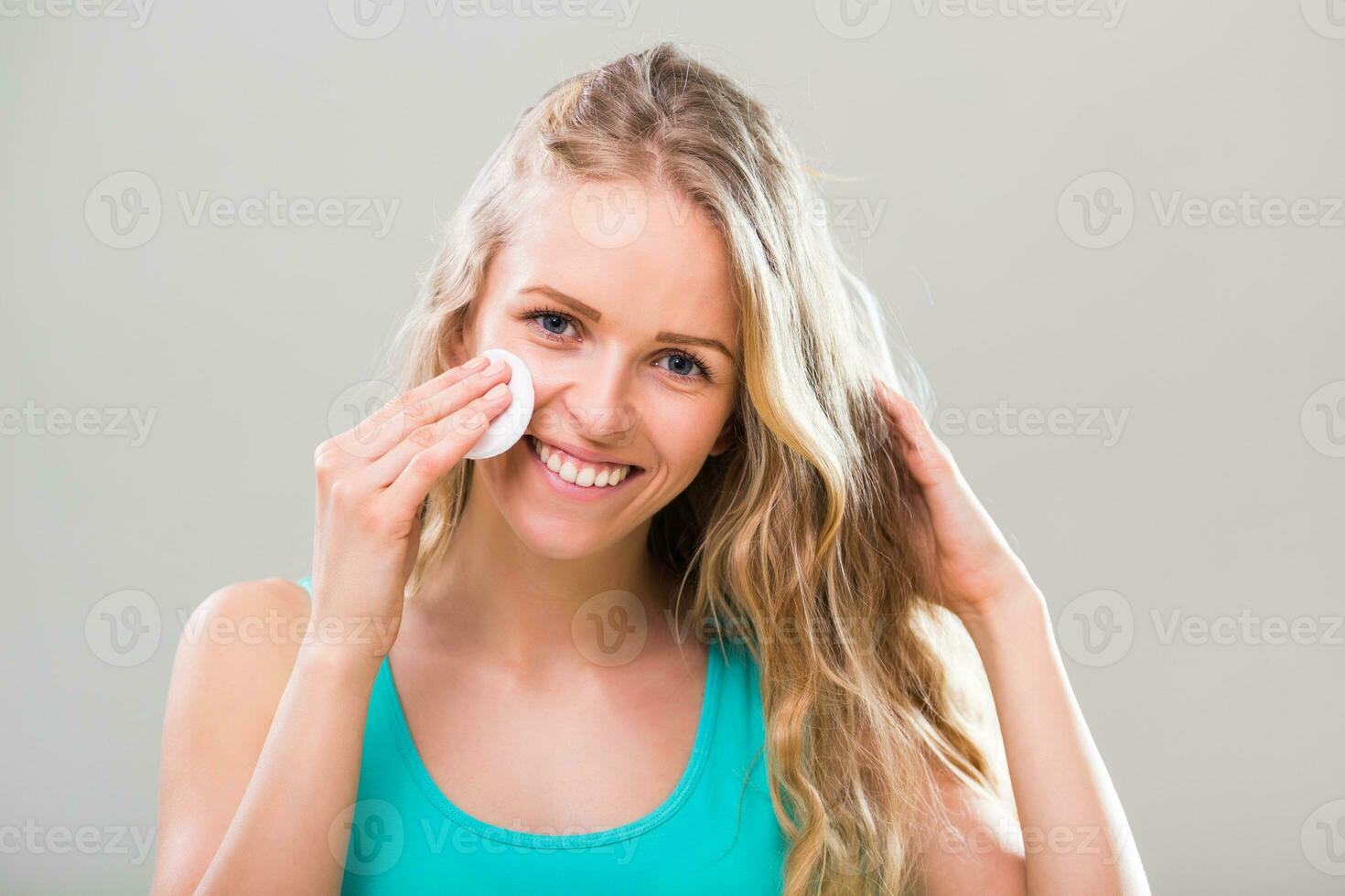 schön jung Frau Reinigung ihr Gesicht mit Baumwolle Pad auf grau Hintergrund. foto