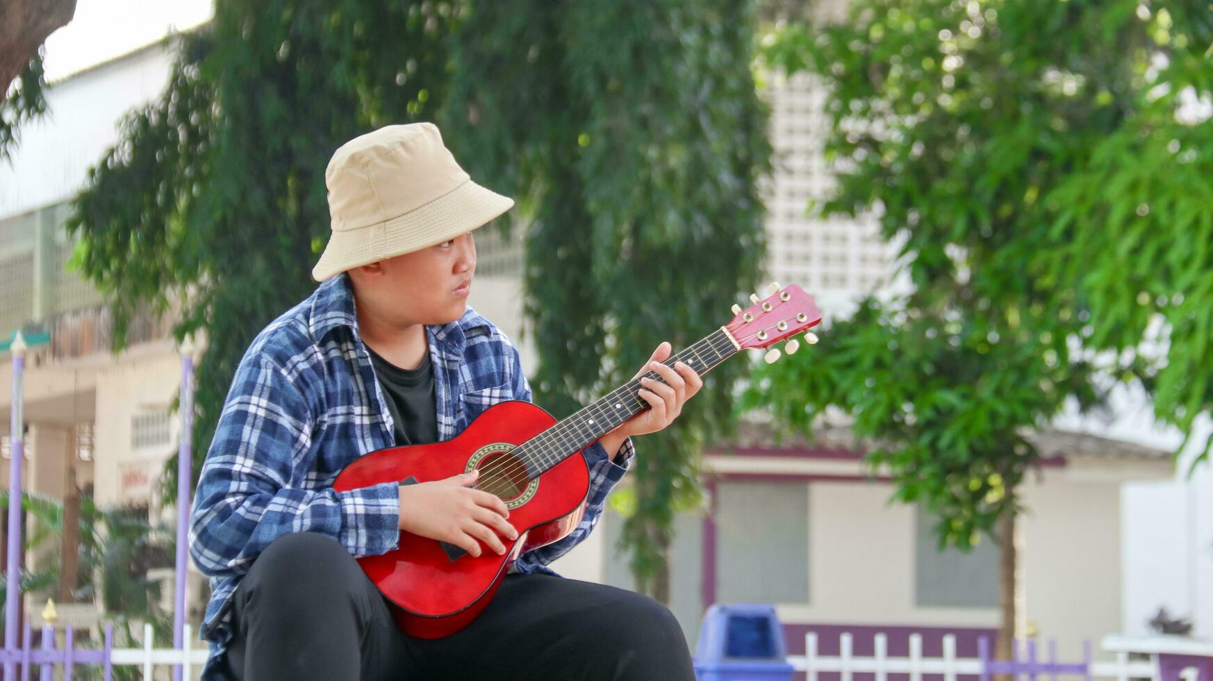 jung asiatisch Junge ist spielen Gitarre im ein lokal Park, Sanft und selektiv Fokus foto