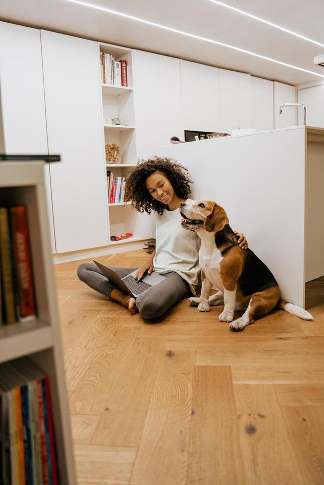 schwarze junge frau, die laptop benutzt und ihren hund streichelt foto