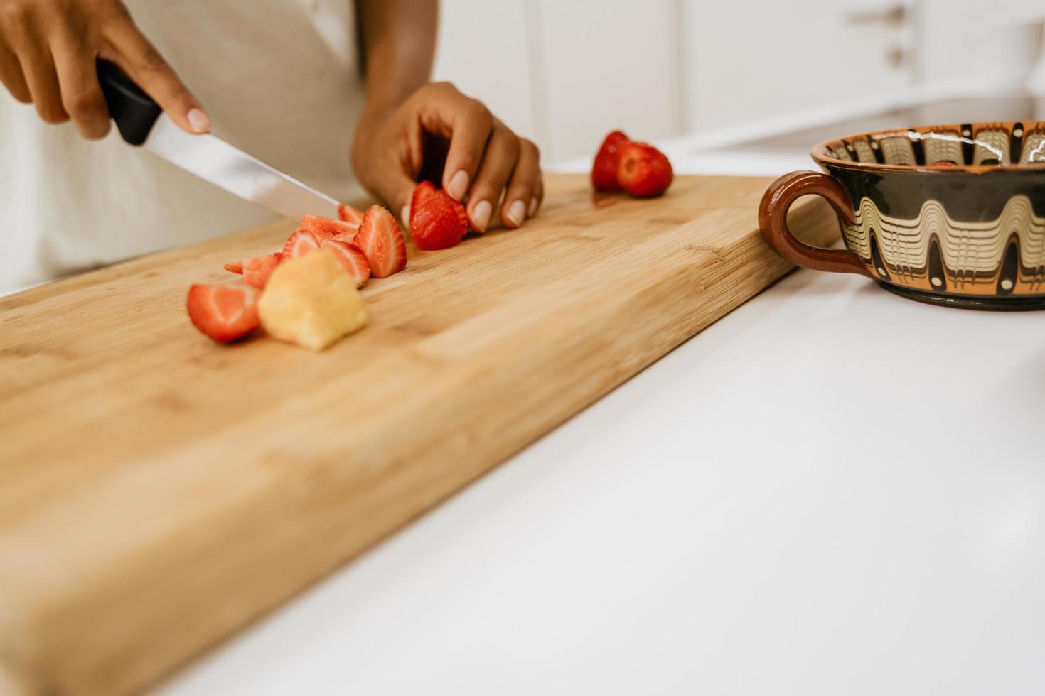 Schwarze junge Frau, die Erdbeeren schneidet, während sie Salat in der Küche macht foto